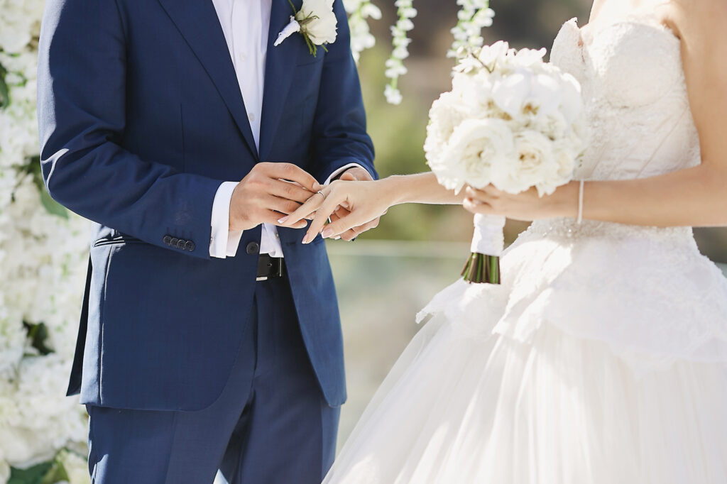 Hands with wedding rings modish groom putting golden ring bride s finger wedding ceremony loving couple woman wedding dress handsome man stylish blue suit