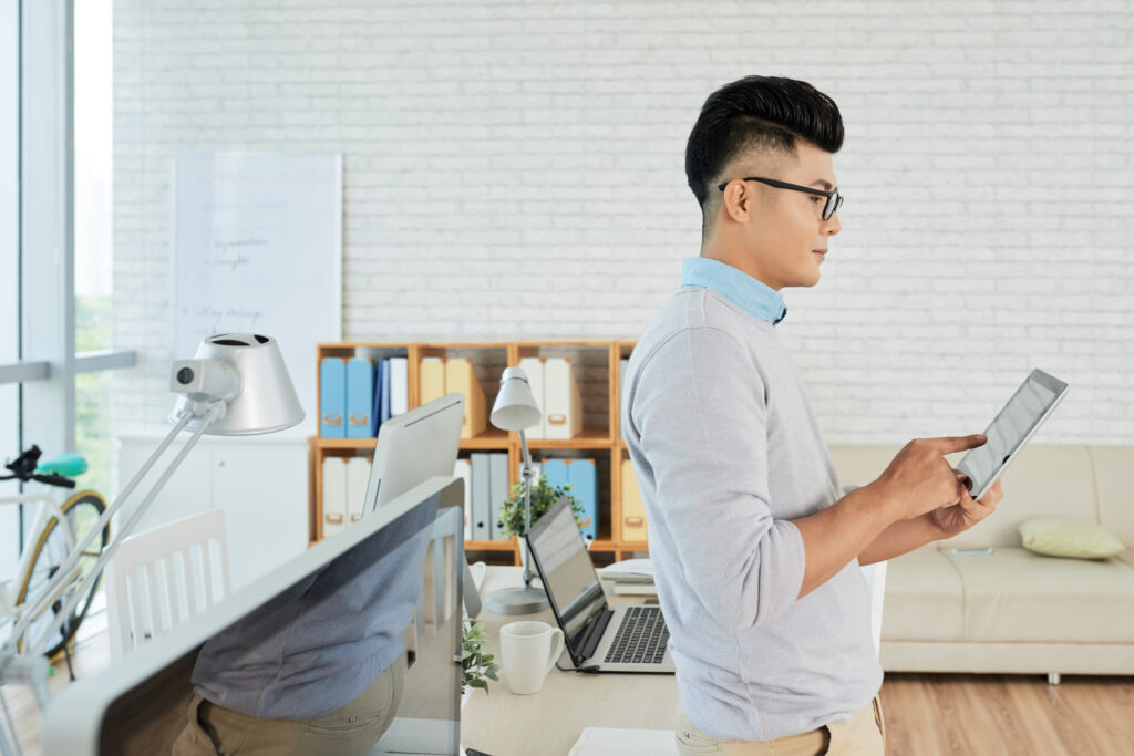 Young manager standing at office and typing on touchpad