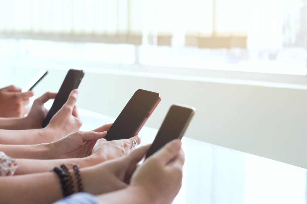 Cropped hands friends using phones against window